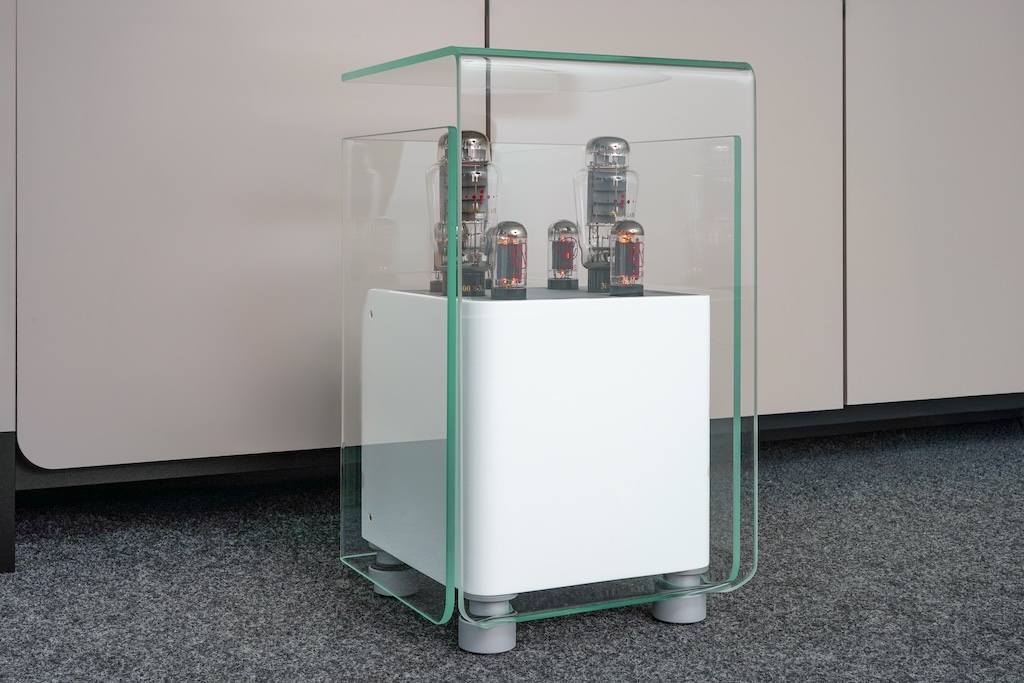 Mit seinem Röhren-Ensemble liefert der Verstärker 36 Watt – in reinem Class-A-Betrieb. Zur Reinheit der Wiedergabe ist die durchsichtige Glaseinhüllung das optisch Pendant. Die verschachtelten, u-förmigen Glasgebilde erfüllen gleich mehrere Aufgabe: Sie dienen als Schutz für und vor den Röhren. Zugleich ermöglichen sie einen freien Blick auf das oberseitig inszenierte Glimmkolben-Ensemble. Durch ihre Formgebung und die Freiräume sorgen sie für einen definierten Kamin-Effekt zur Abführung der Wärme, was den Röhren und der Verstärkerschaltung eine konstante Betriebstemperatur beschert. Zudem bewirken sie ein Verschlankung des eigentlich kompakt-quaderförmigen Verstärkers und befördern seine luftige Erscheinung.