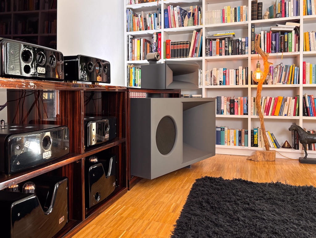 Das untere Lautsprecher-Gehäuse bietet in einem Korpus die Kombination von Mitteltieftöner und Subwoofer. Der Mitteltieftöner ist wiederum als Horn ausgelegt, der Subwoofer hingegen als konventioneller Konus-Lautsprecher. Das Gehäuse dieser Kombination wird von dem geschwungenen Rahmen luftig eingefasst. Auch die Elektronik ist in einem eigenen Element dieser Rahmenkonstruktion eingepasst, so bilden Lautsprecher und Elektronik eine stimmige Einheit. In diesem Board sind in der mittleren Ebene auch die beiden Hybridverstärker untergebracht, welche die Woofer beider Systemseiten aktiv antreiben.